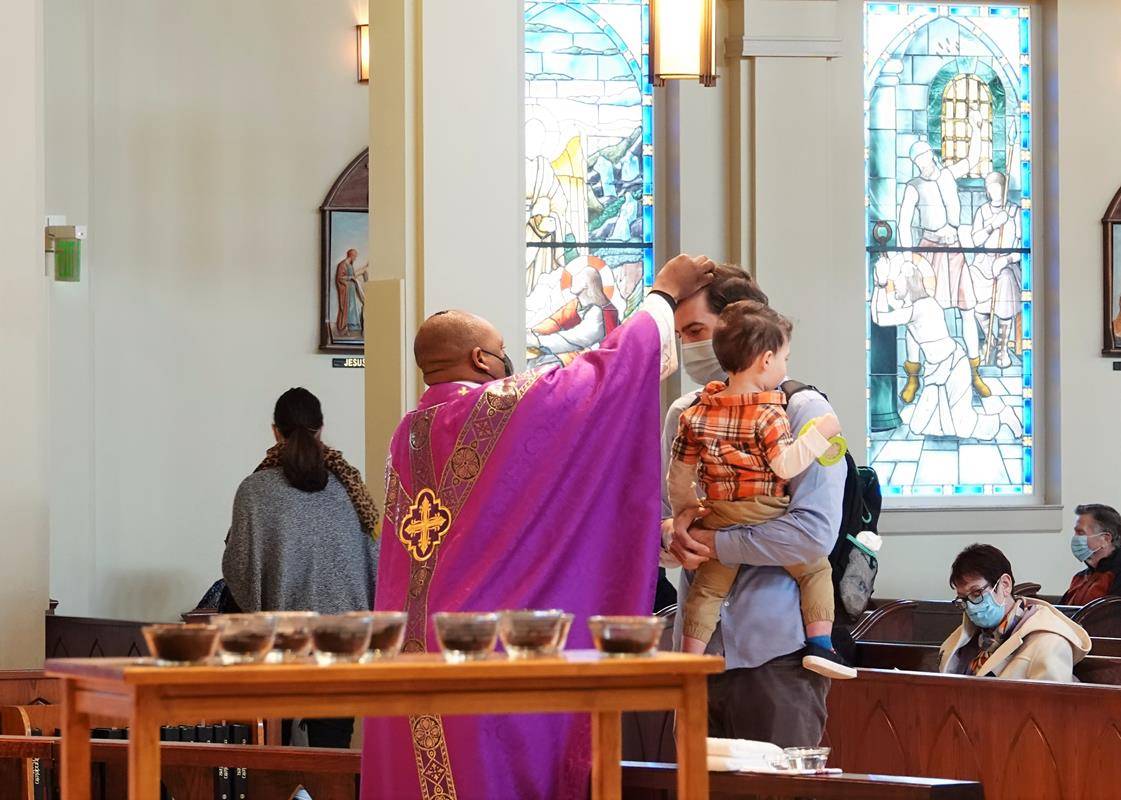 HUNTERSVILLE — Father Melchesideck Yumo distributes ashes to Colin Riggles and his son Carter at St. Mark Church in Huntersville. (Photos provided by Amy Burger.)